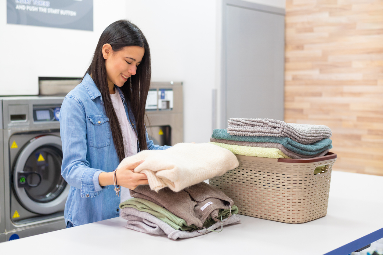 Young smiling woman washing her clothes in the washing machine in the laundromat