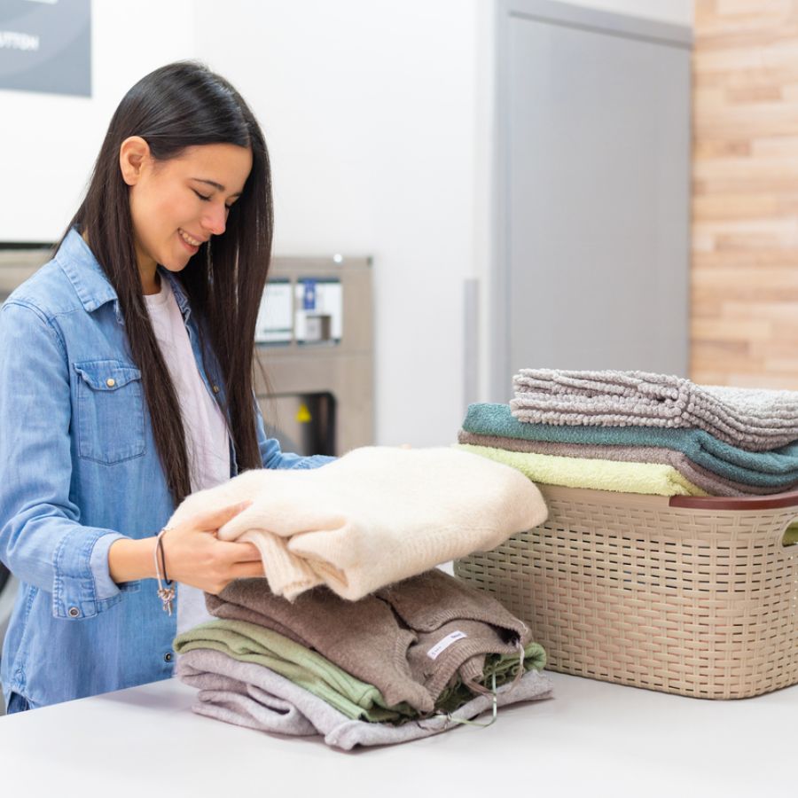 Young smiling woman washing her clothes in the washing machine in the laundromat 